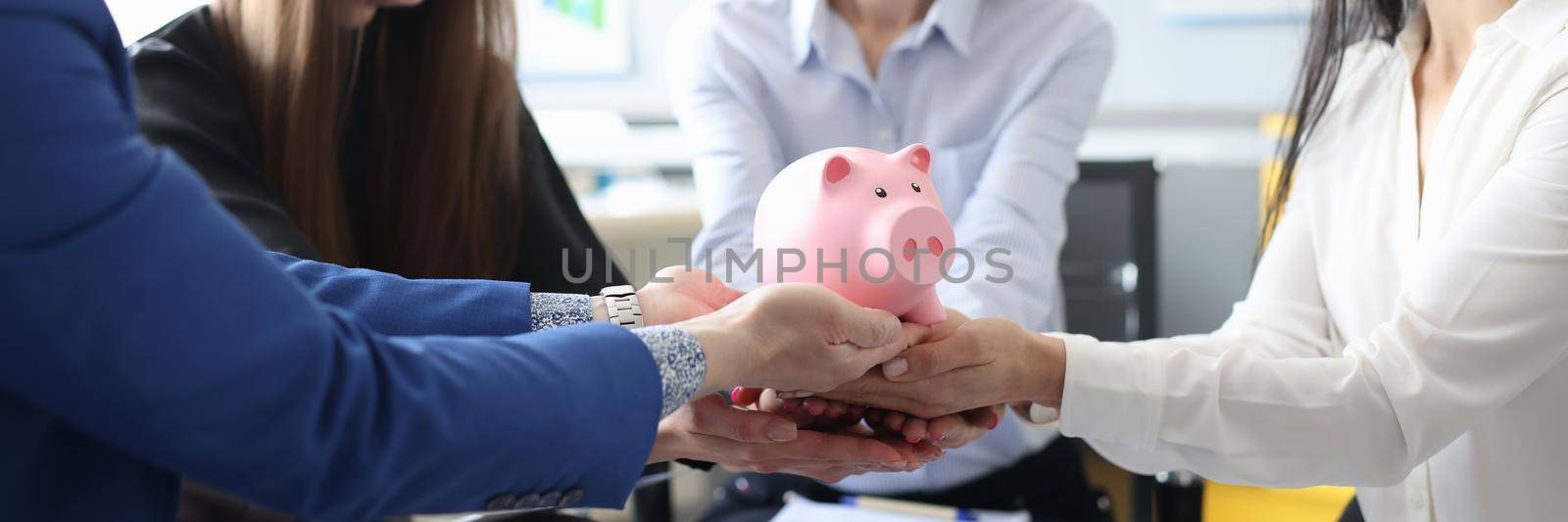 Group of people holding a piggy bank together in the office by kuprevich