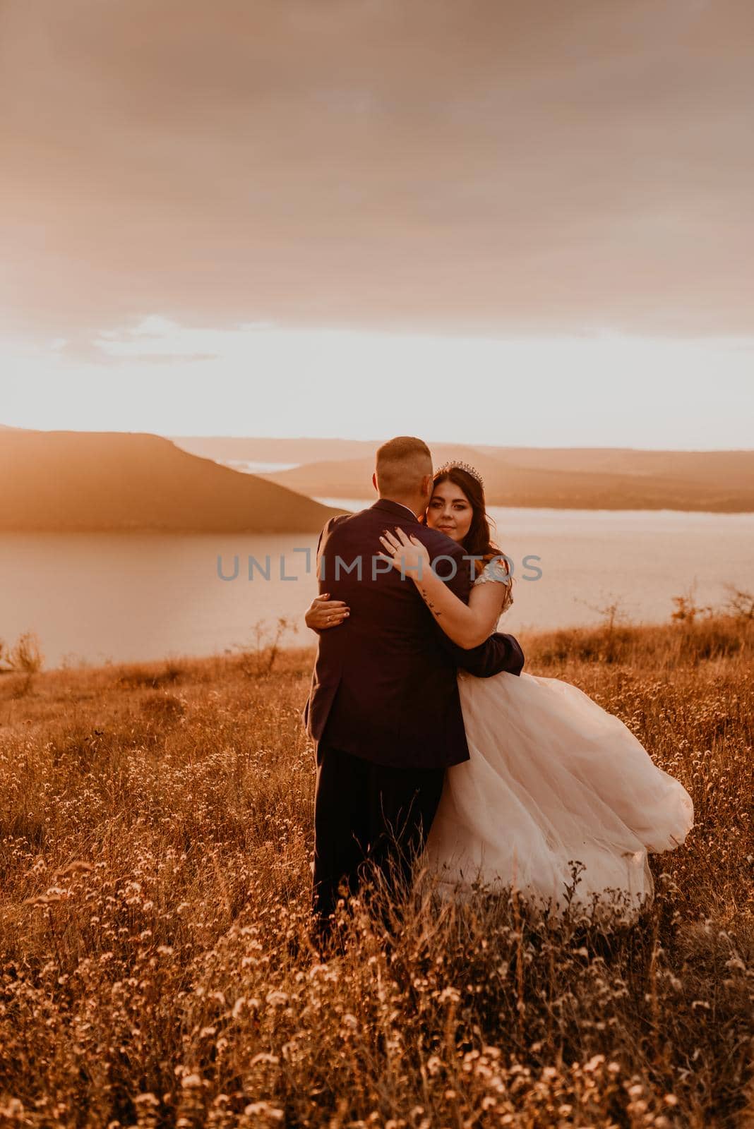 loving couple wedding newlyweds hug kissing in summer field on mountain above the river by AndriiDrachuk