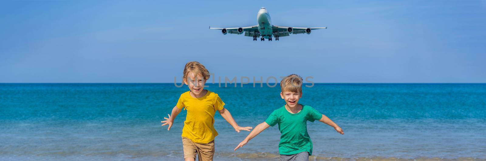 Two happy boys have fun on the beach watching the landing planes. Traveling on an airplane with kids concept. Text space. Island Phuket in Thailand. Impressive paradise. Hot beach Mai Khao. Amazing landscape. BANNER, LONG FORMAT