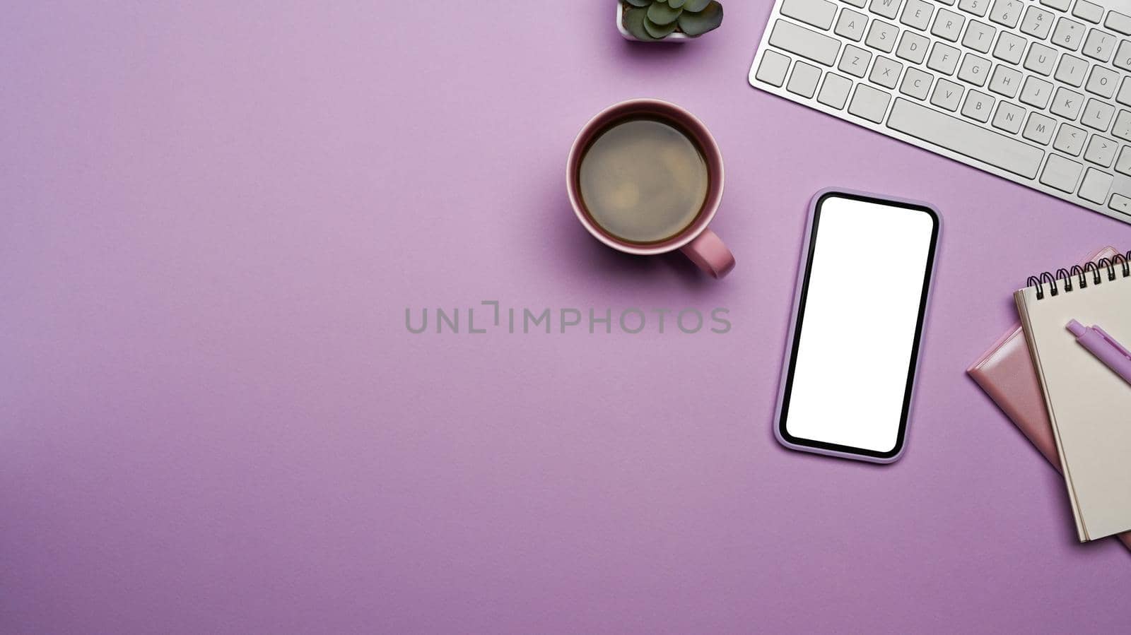 Mobile phone with blank screen, coffee cup and supplies on purple background.