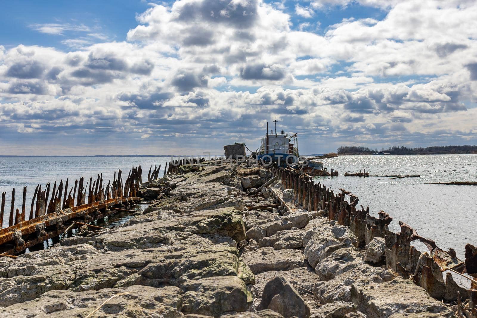 An old abandoned stone pier goes into the sea. An old ship is moored. A sunny day with clouds in Baltiysk, Kaliningrad region, Russia, near the Baltic sea.