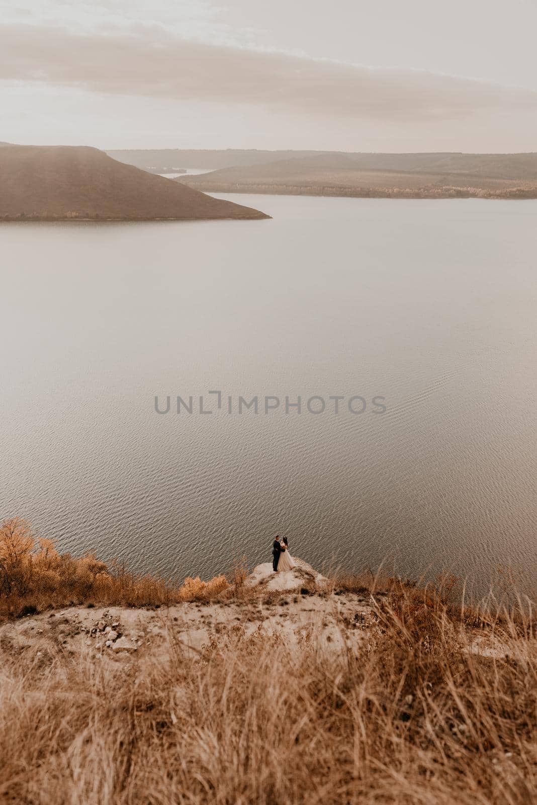 a wedding couple in love, the groom and the bride stand on the Big Stone on the cliff and kiss. panoramic view big river lake sea in distance silhouettes of the islands