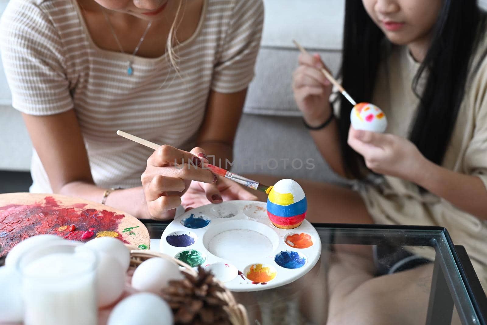 Smiling young woman with little cute girl are coloring eggs preparing for Easter celebration.