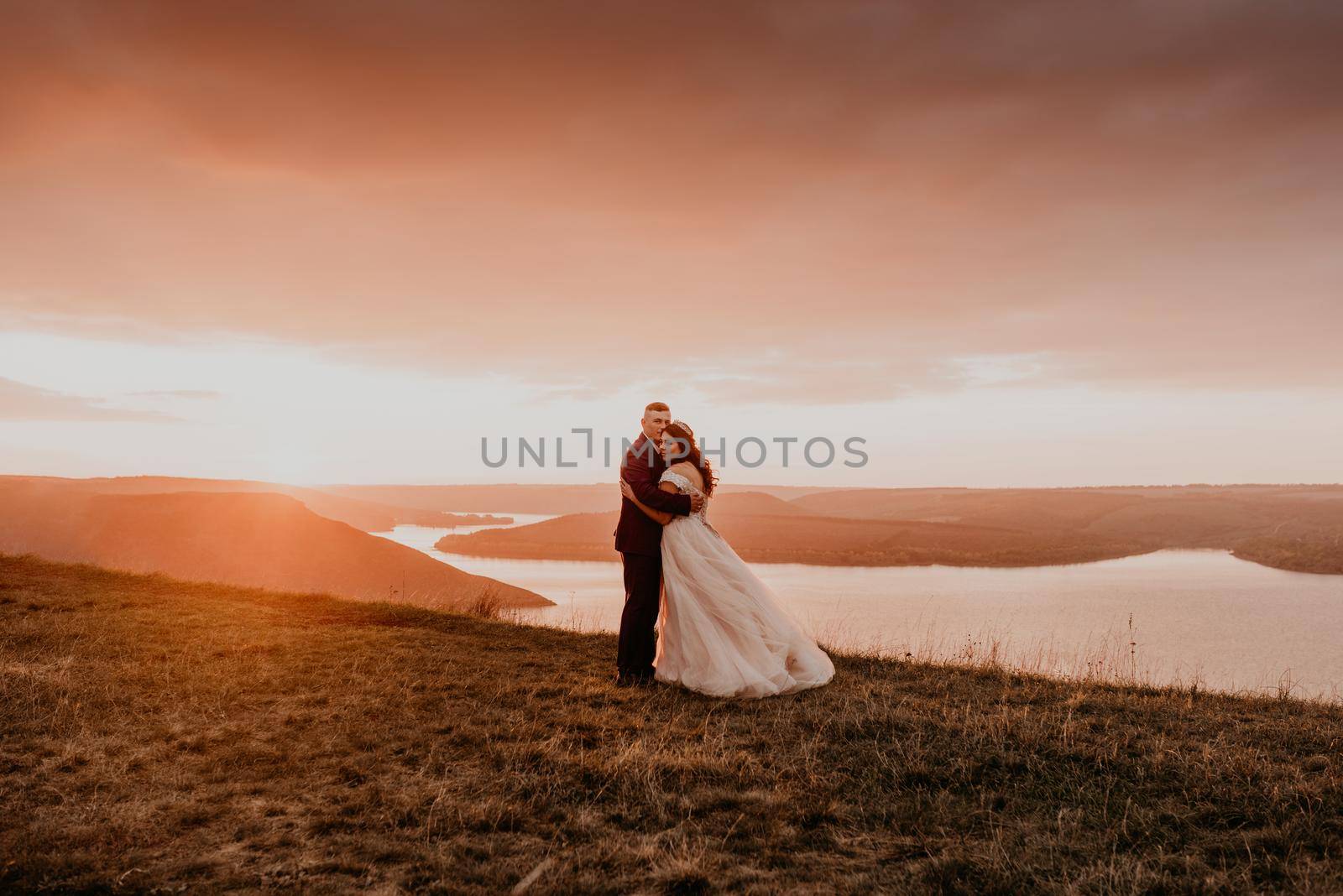 A loving couple wedding newlyweds walk in tsummer in the fall on mountain on cliff above the river. sunset. bride in a white dress with crown on her head. style fashionable women hairstyle makeup