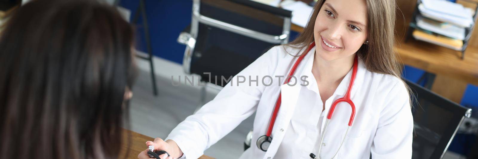 Young female doctor measures blood pressure to a patient. Preliminary health examination before visiting the clinic, health card