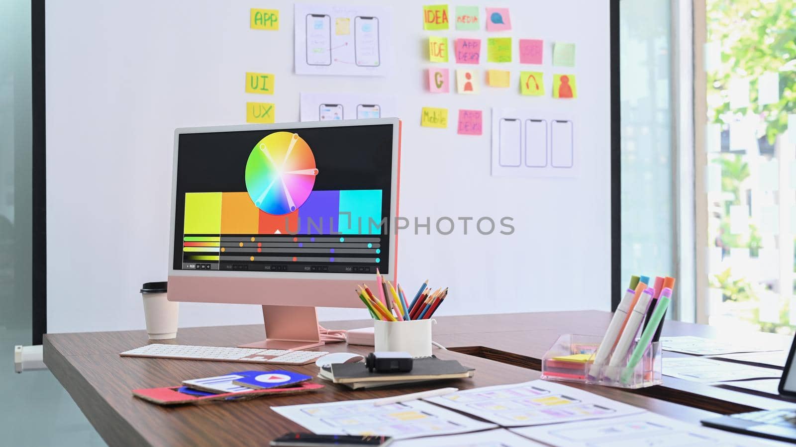 Modern computer with color swatches and wireframe sketches for mobile application on wooden table.