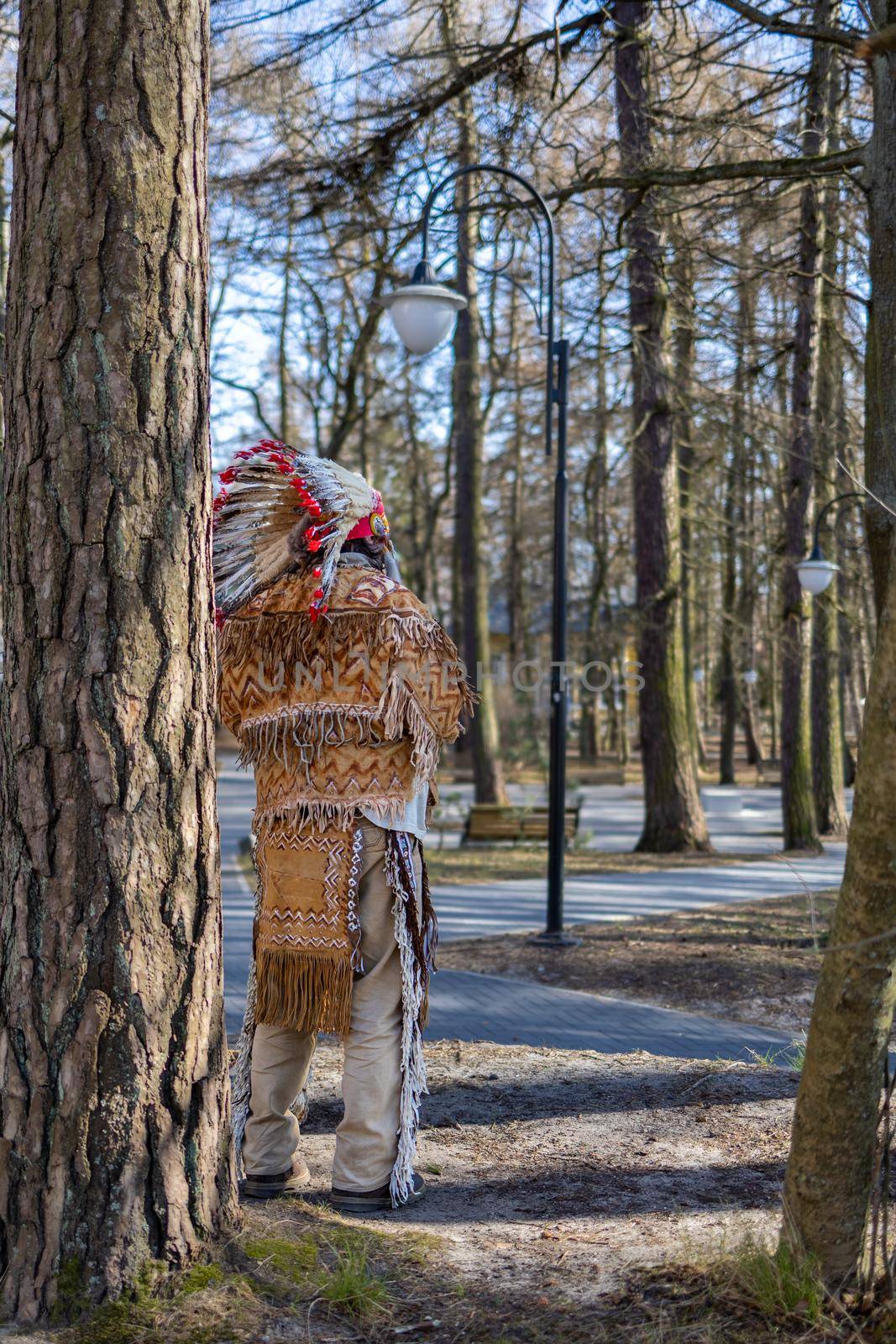 An Indian Native American in a national costume stands in the park among the trees in Svetlogorsk Raushen, Kalinigrad region, Russia, near the Baltic sea. High quality photo.
