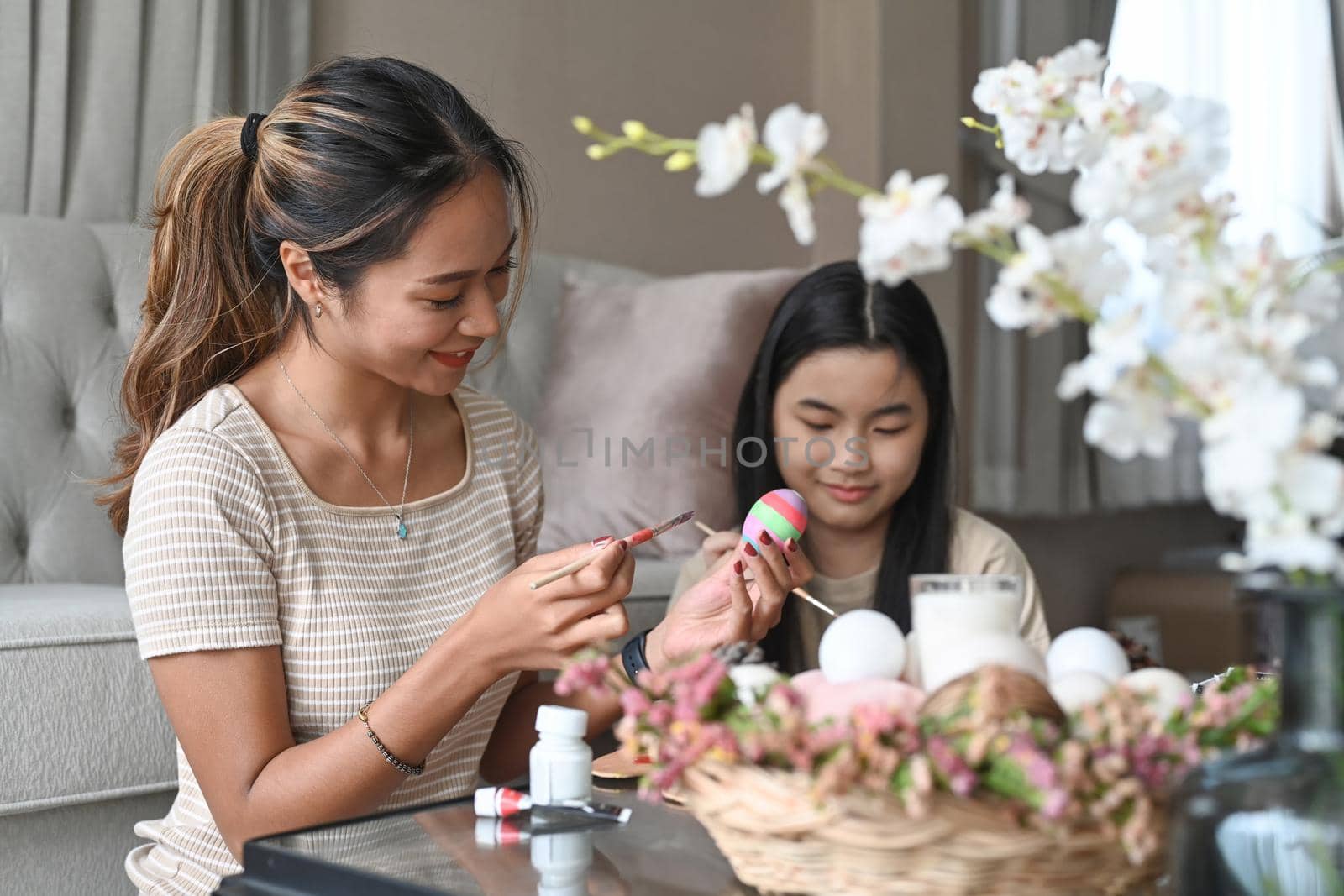 Beautiful asian mother and her daughter painting Easter eggs together. Happy family preparing for Easter day.