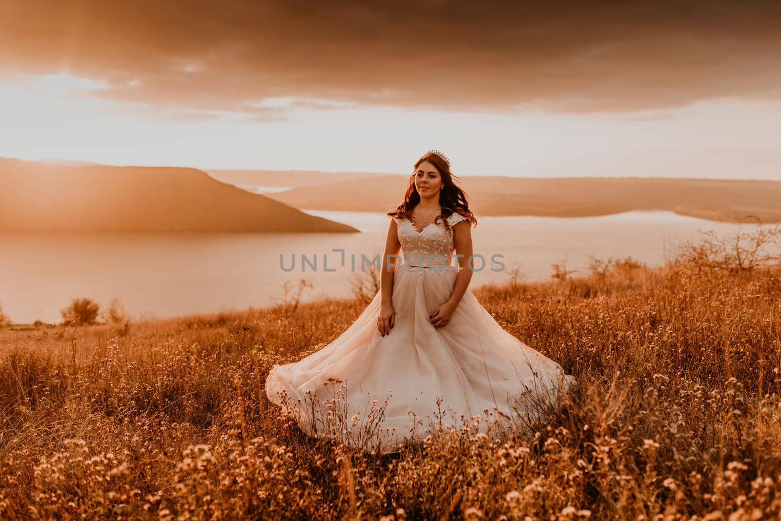 beautiful woman brunette bride in white dress and suit are walking on tall grass in field in summer