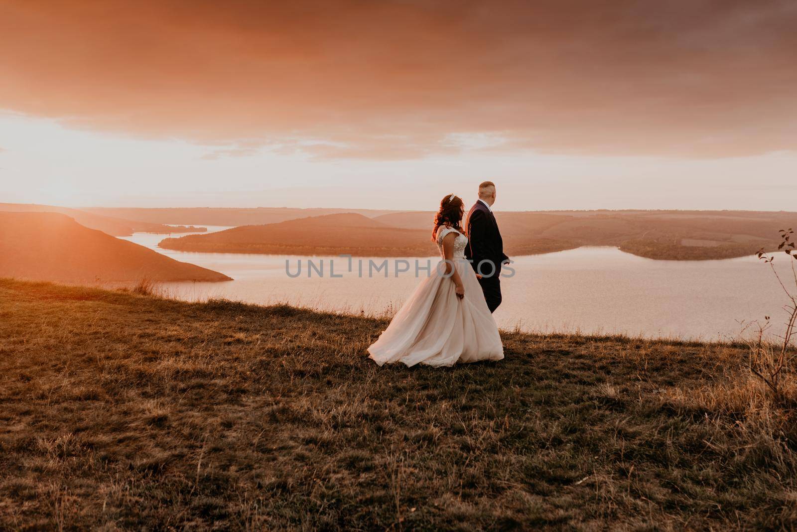 loving couple wedding newlyweds walk in tsummer in the fall on mountain above the river. sunset. by AndriiDrachuk