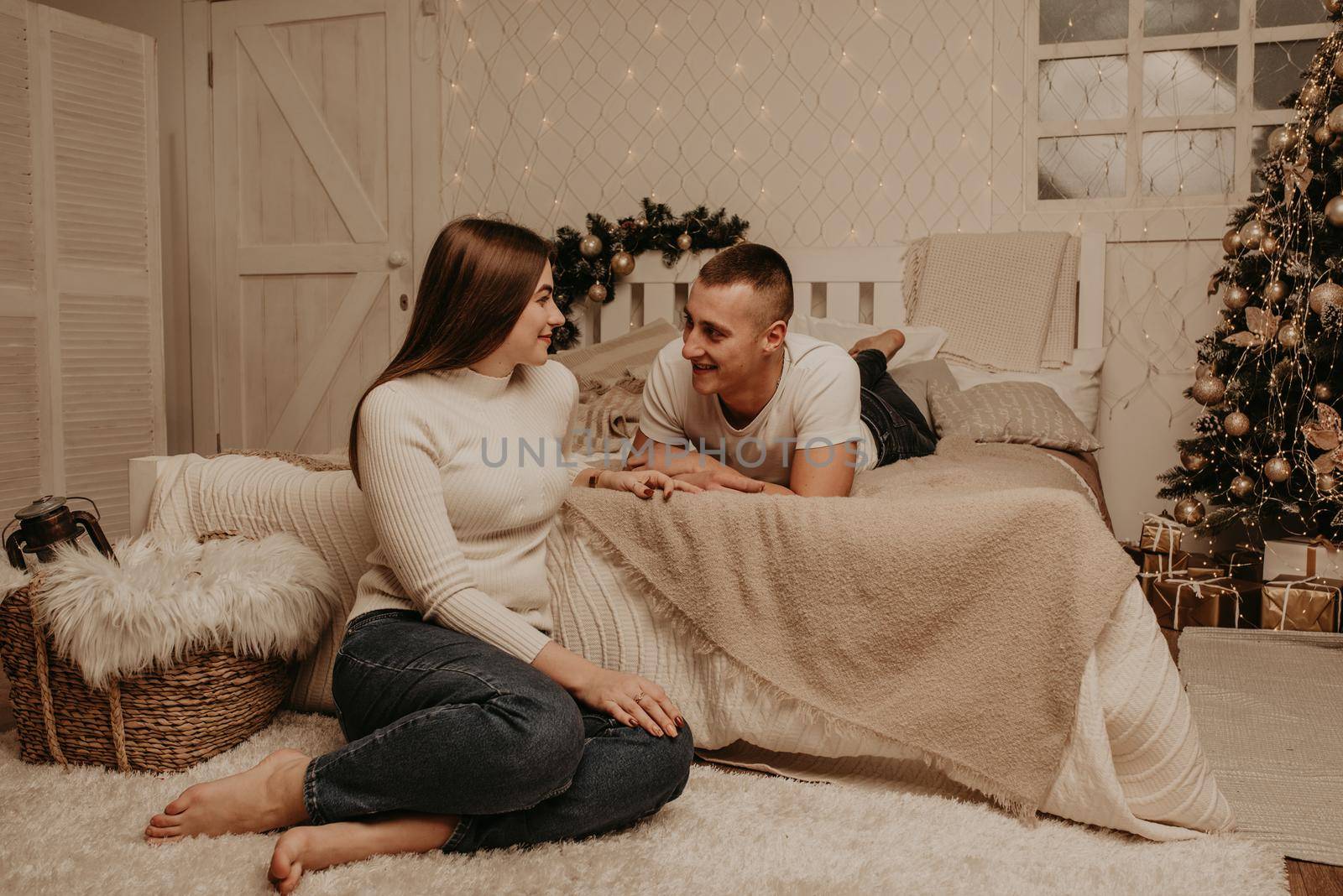 couple man and woman lie on bed bedroom near christmas tree.decorated house for New Year.Christmas morning. apartment interior. Valentine's Day celebration