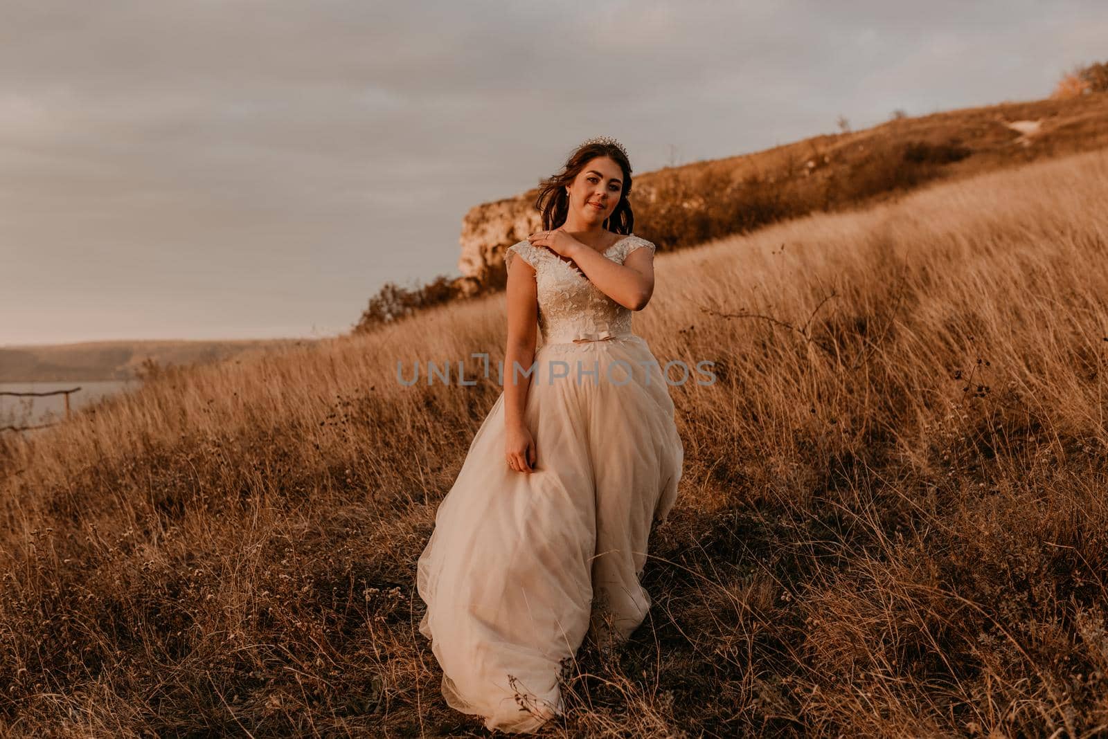 beautiful woman brunette bride in white dress and suit are walking on tall grass in field in summer