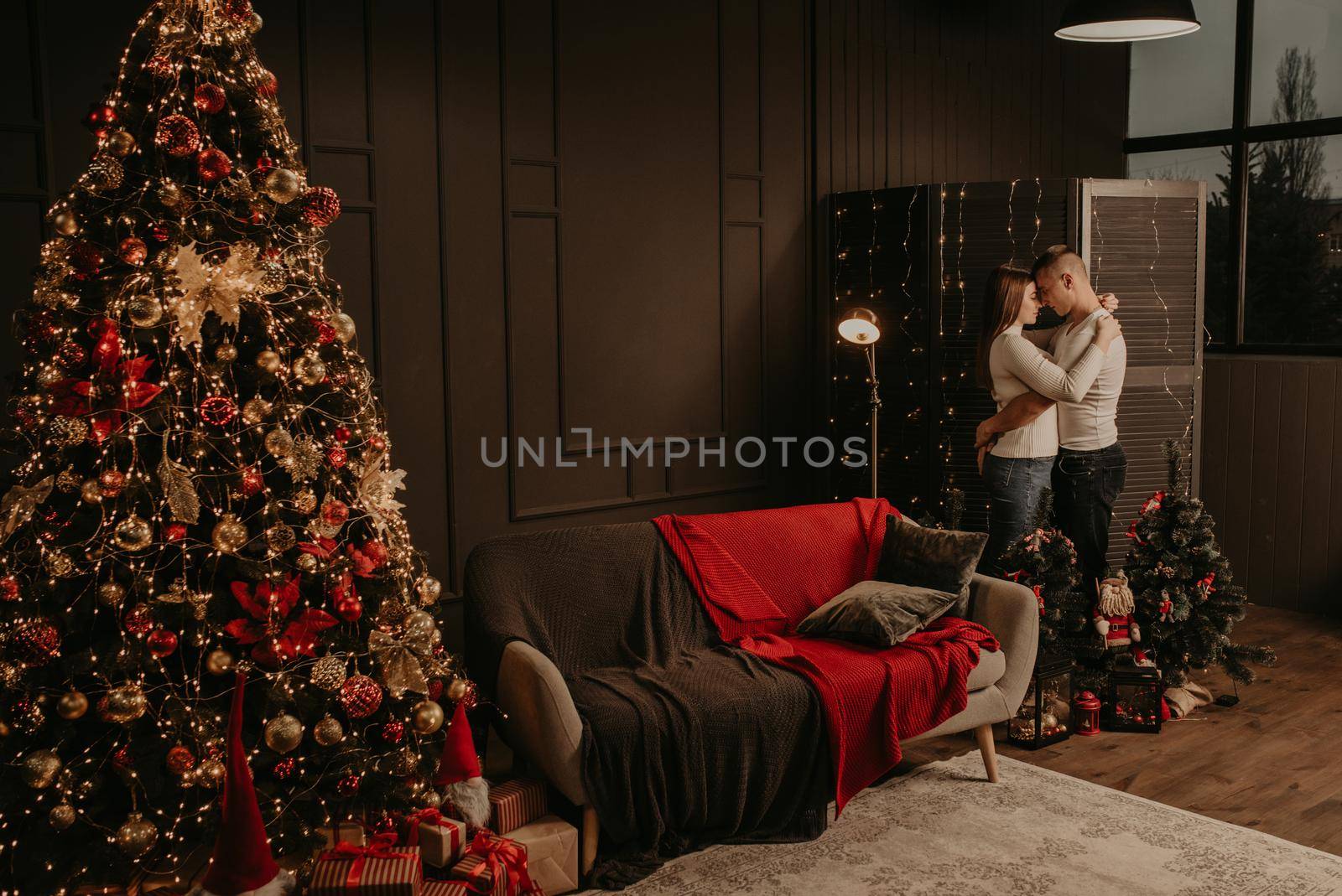 love young couple man and woman hugging kissing near a Christmas tree. decorated house for New Year. Christmas morning. apartment interior. Valentine's Day celebration