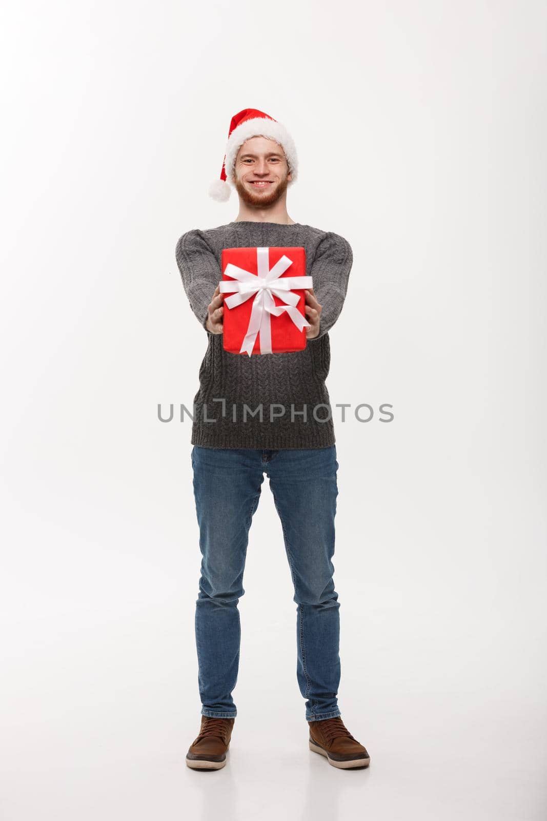 Christmas Concept - Happy young handsome man with beard giving presents to camera isolated on white background.