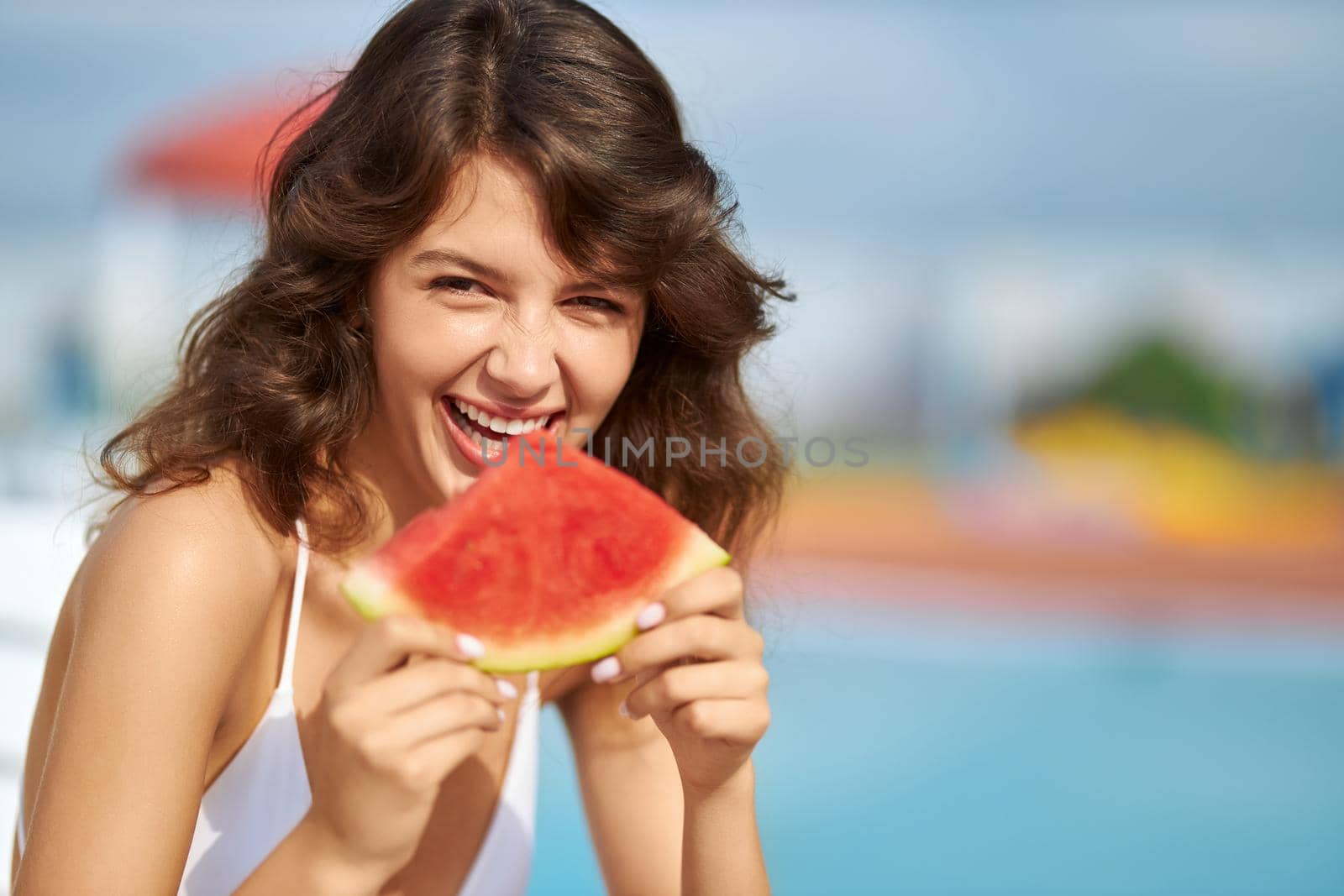 Happy wavy haired female smiling in pleasure, while biting watermelon outside. by SerhiiBobyk