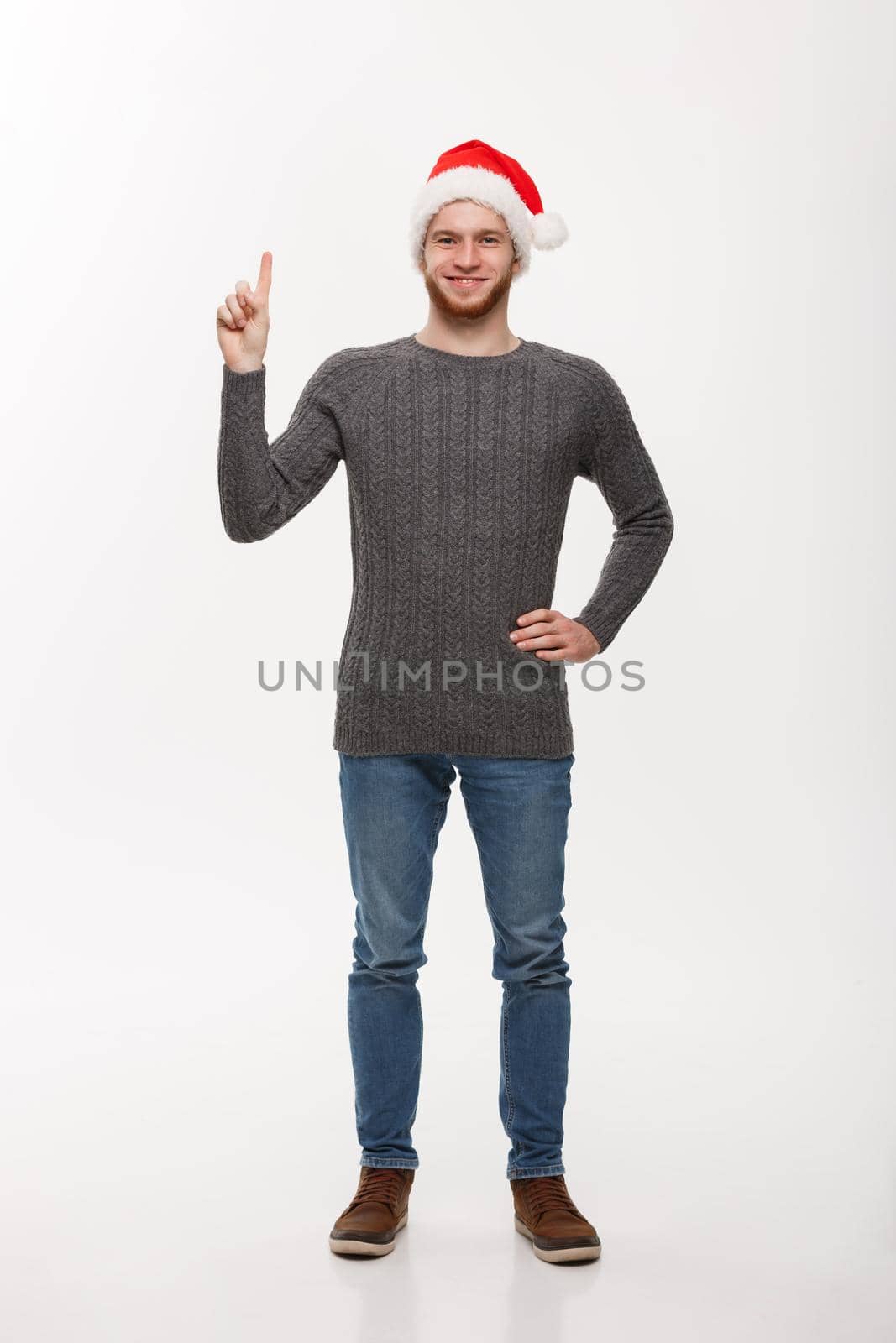 Holiday Concept - Young beard man in sweater enjoy playing and pointing finger upward.