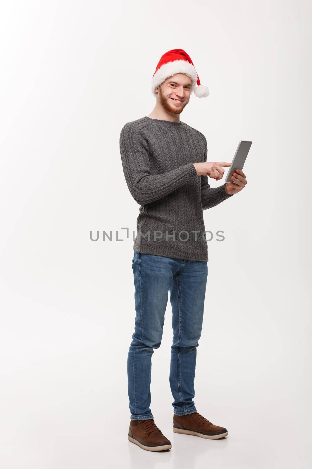 Holiday concept - Young beard handsome man working on digital tablet over white background. by Benzoix