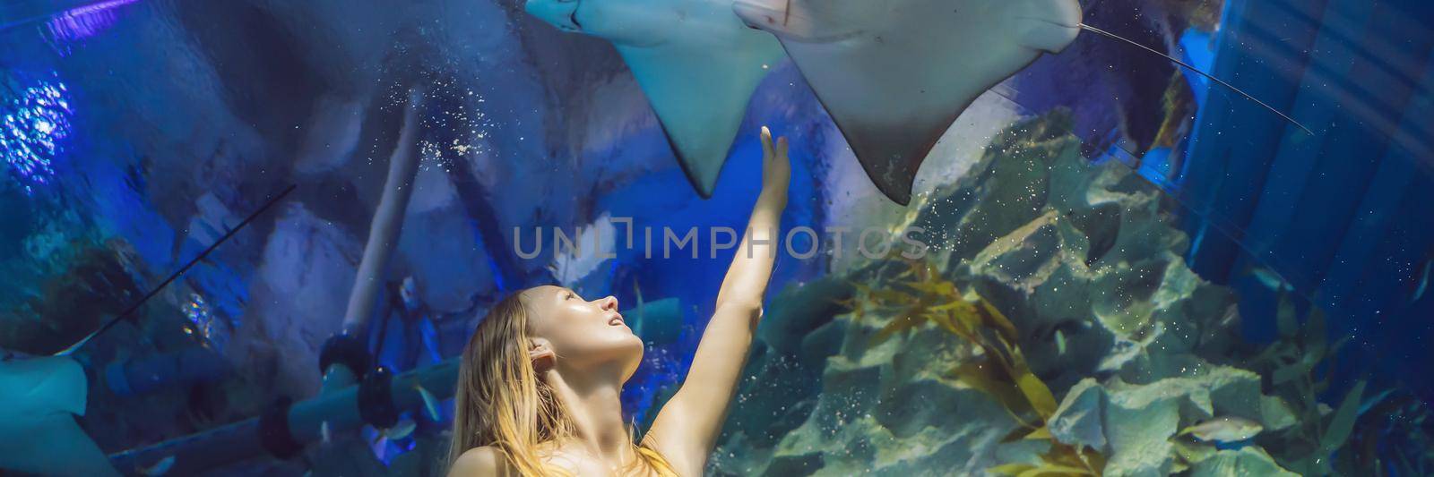 Young woman touches a stingray fish in an oceanarium tunnel. BANNER, LONG FORMAT