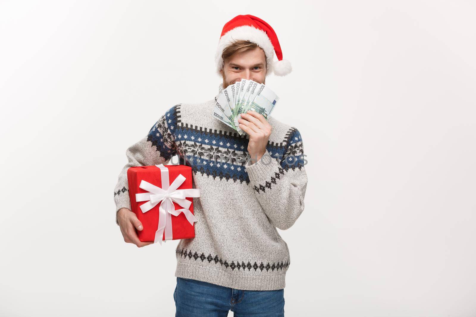 Holiday Concept - young beard man holding a christmas gift box and money over white background