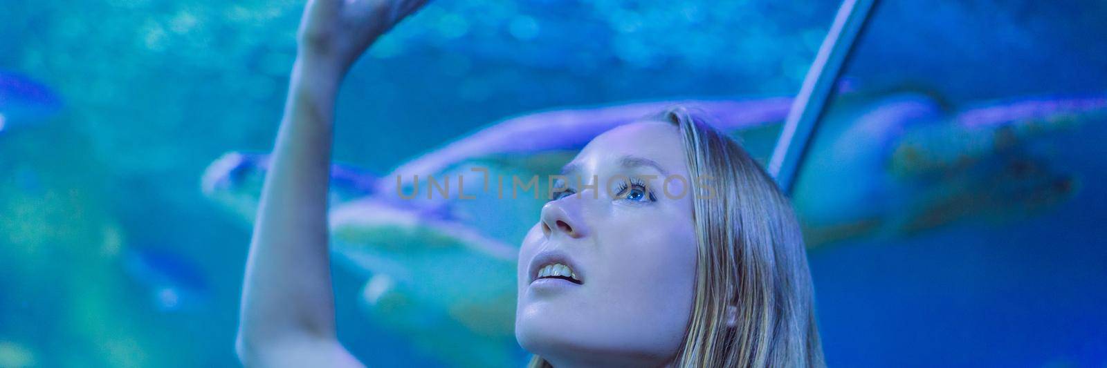 Young woman touches a stingray fish in an oceanarium tunnel. BANNER, LONG FORMAT