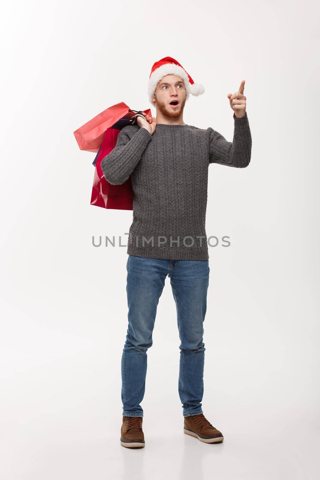 Christmas Concept - attractive young caucasian man surprising shocking holding shopping bag and pointing finger in front.