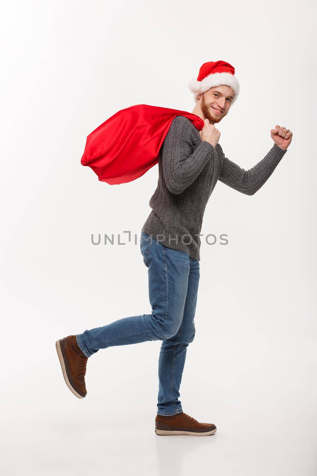 Christmas concept - Young confident beard man running and holding red big santa bag with a lot of present inside.