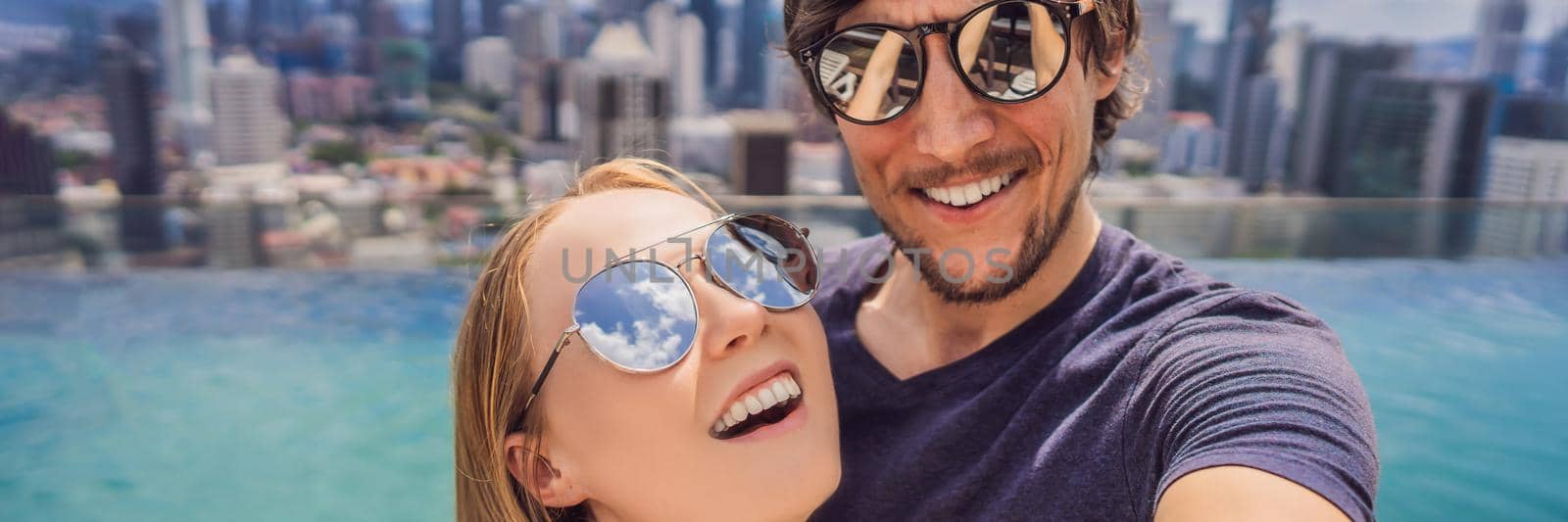 BANNER, LONG FORMAT young happy and attractive playful couple taking selfie picture together at luxury urban hotel infinity pool and panoramic view of the city enjoying holidays honeymoon travel in diversity ethnicity and love.