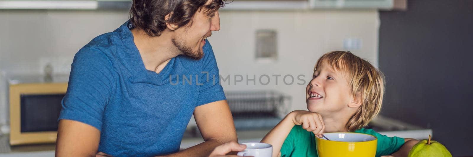 Father and son are talking and smiling while having a breakfast in kitchen BANNER, LONG FORMAT by galitskaya