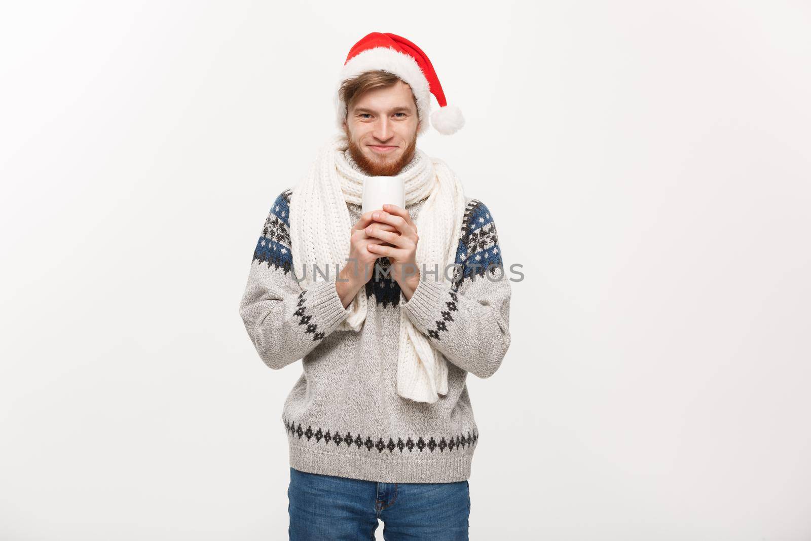 Christmas concept - Young beard man in sweater and santa hat holding a hot coffee cup isolated on white with copy space.