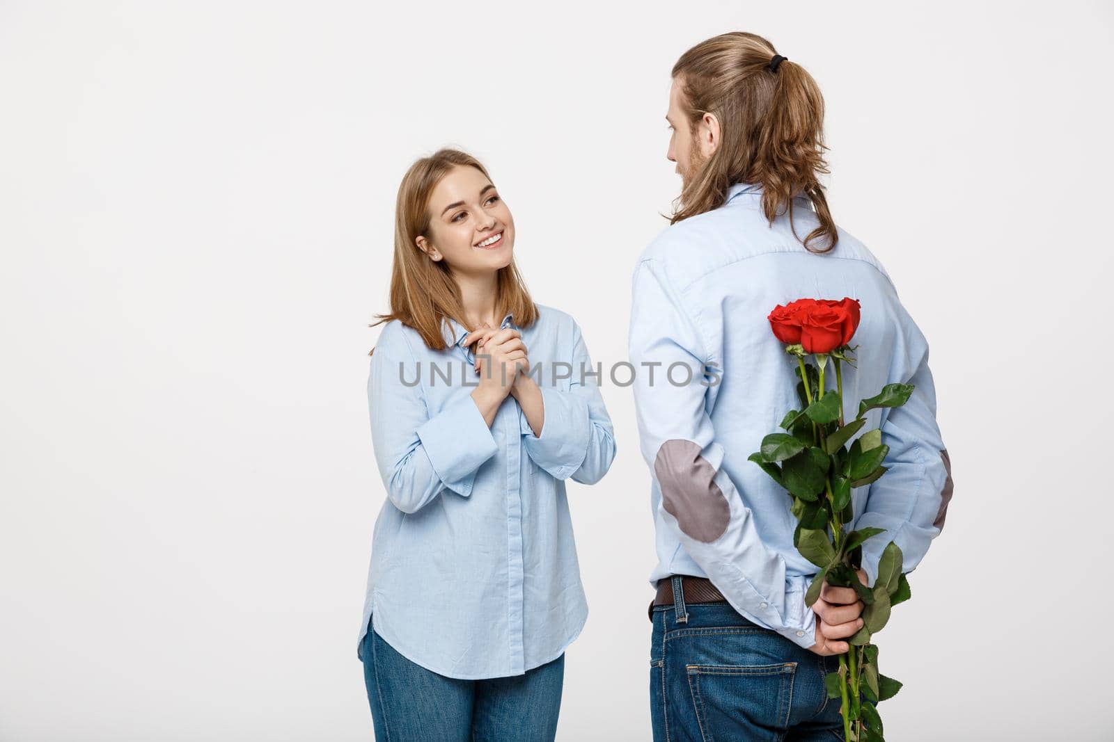 Portrait of handsome elegant guy is surprising his beautiful girlfriend with red roses and smiling over white isolated background .