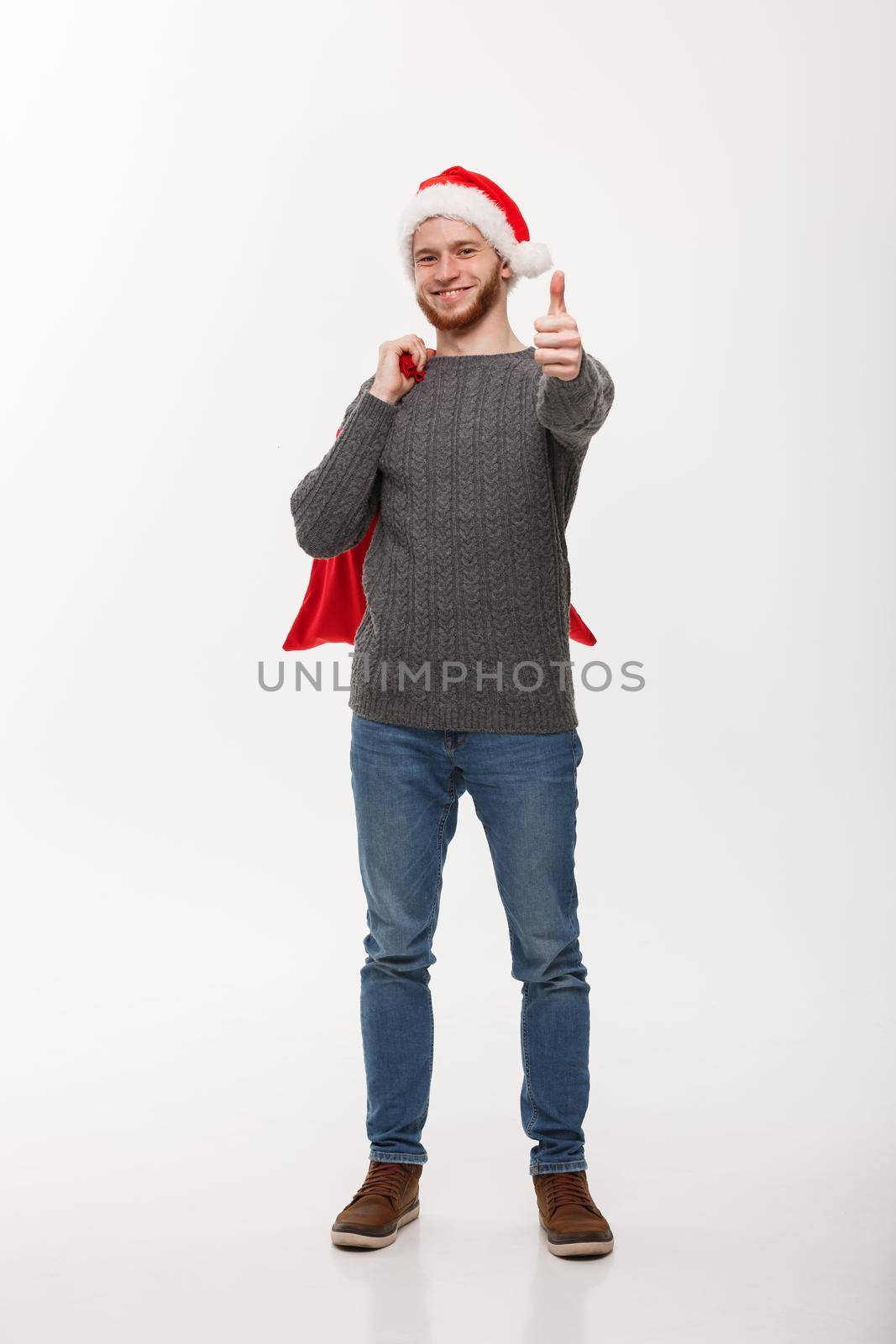 Christmas concept - Young confident smart man holding red big santa bag and giving thumb up.