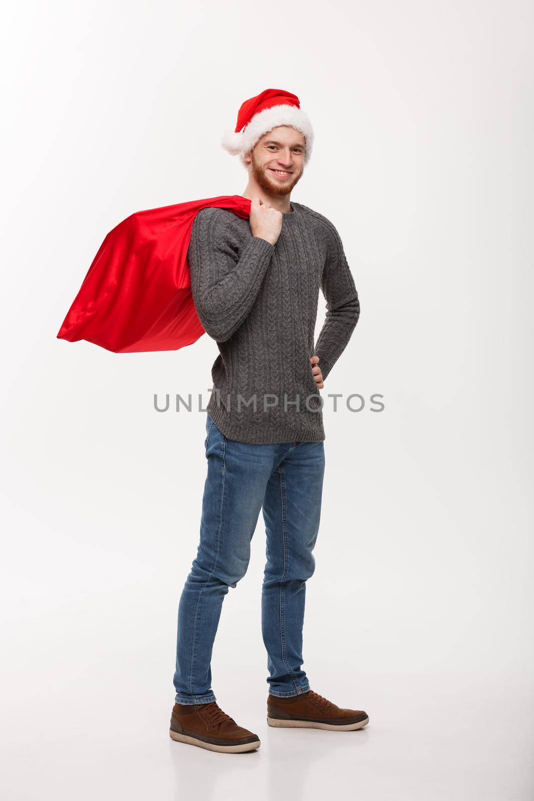 Christmas concept - Young confident smart man holding red big santa bag with a lot of present inside.