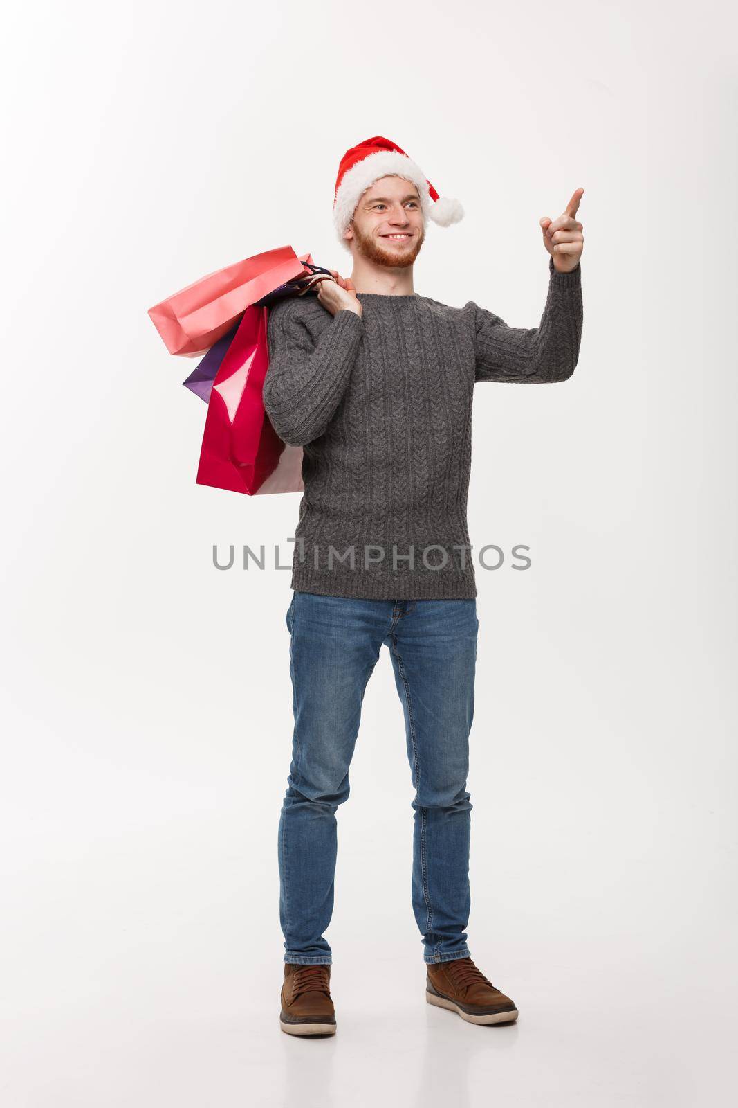 Christmas Concept - attractive young caucasian man surprising shocking holding shopping bag and pointing finger in front.
