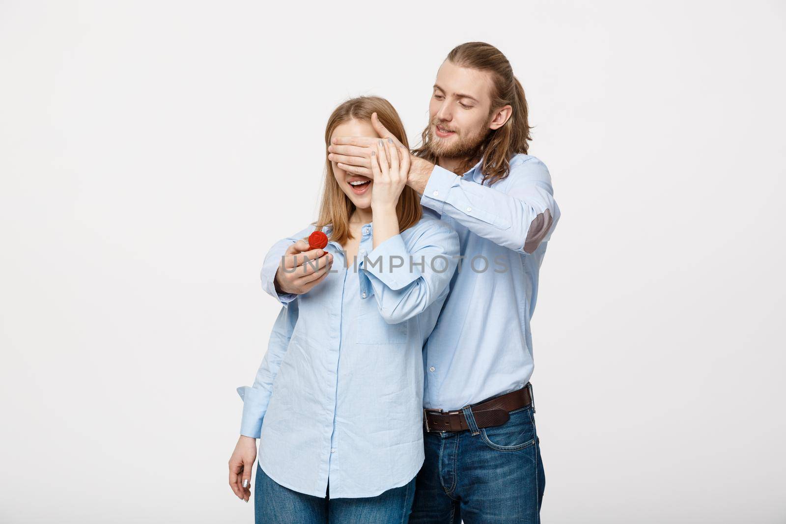 Portrait of handsome beard man hiding his wifes eyes to offer her an engagement ring for a marriage proposal.