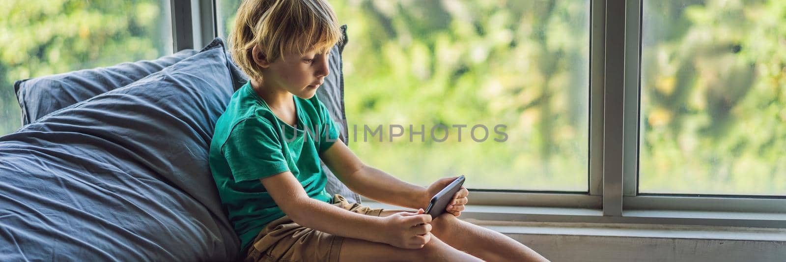 Little blond boy playing games on smartphone. BANNER, LONG FORMAT