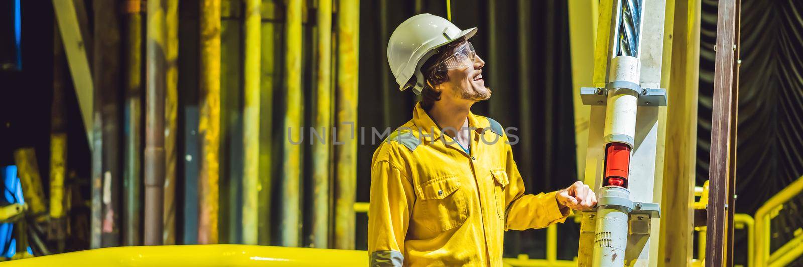 Young man in a yellow work uniform, glasses and helmet in industrial environment,oil Platform or liquefied gas plant. BANNER, LONG FORMAT