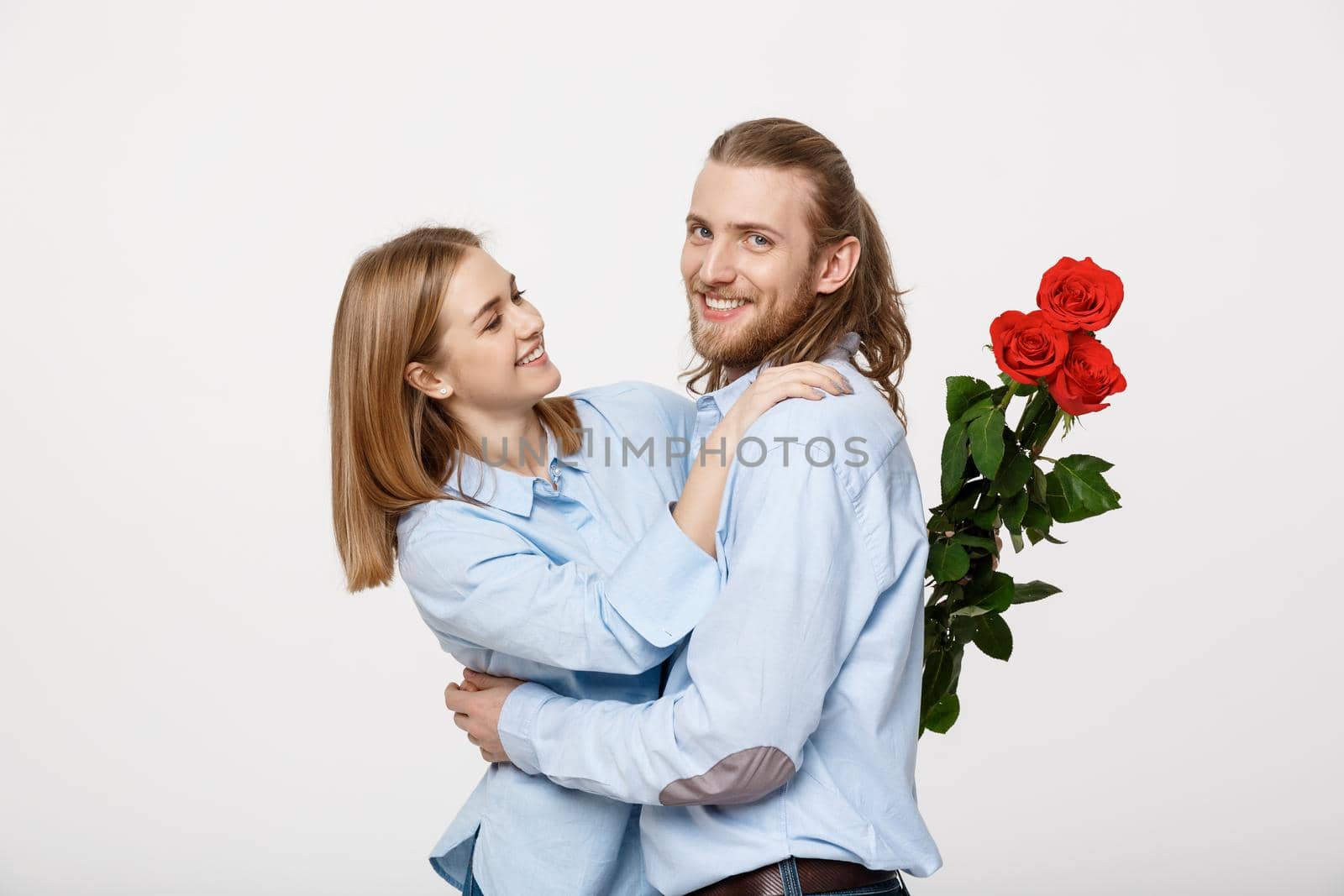 Portrait of an attractive young man hiding flowers from his girlfriend before giving her a surprise over white isolated background .