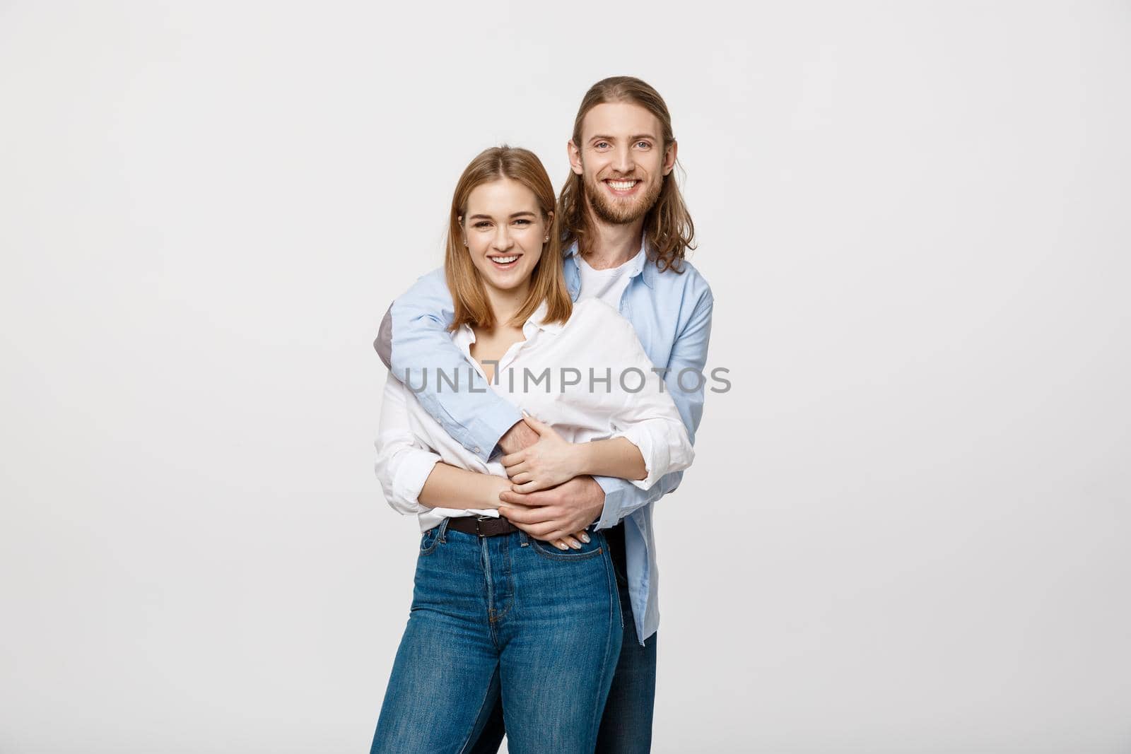 Portrait of cheerful young couple standing and hugging each other on isolated white background.