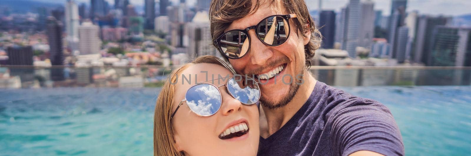 BANNER, LONG FORMAT young happy and attractive playful couple taking selfie picture together at luxury urban hotel infinity pool and panoramic view of the city enjoying holidays honeymoon travel in diversity ethnicity and love.