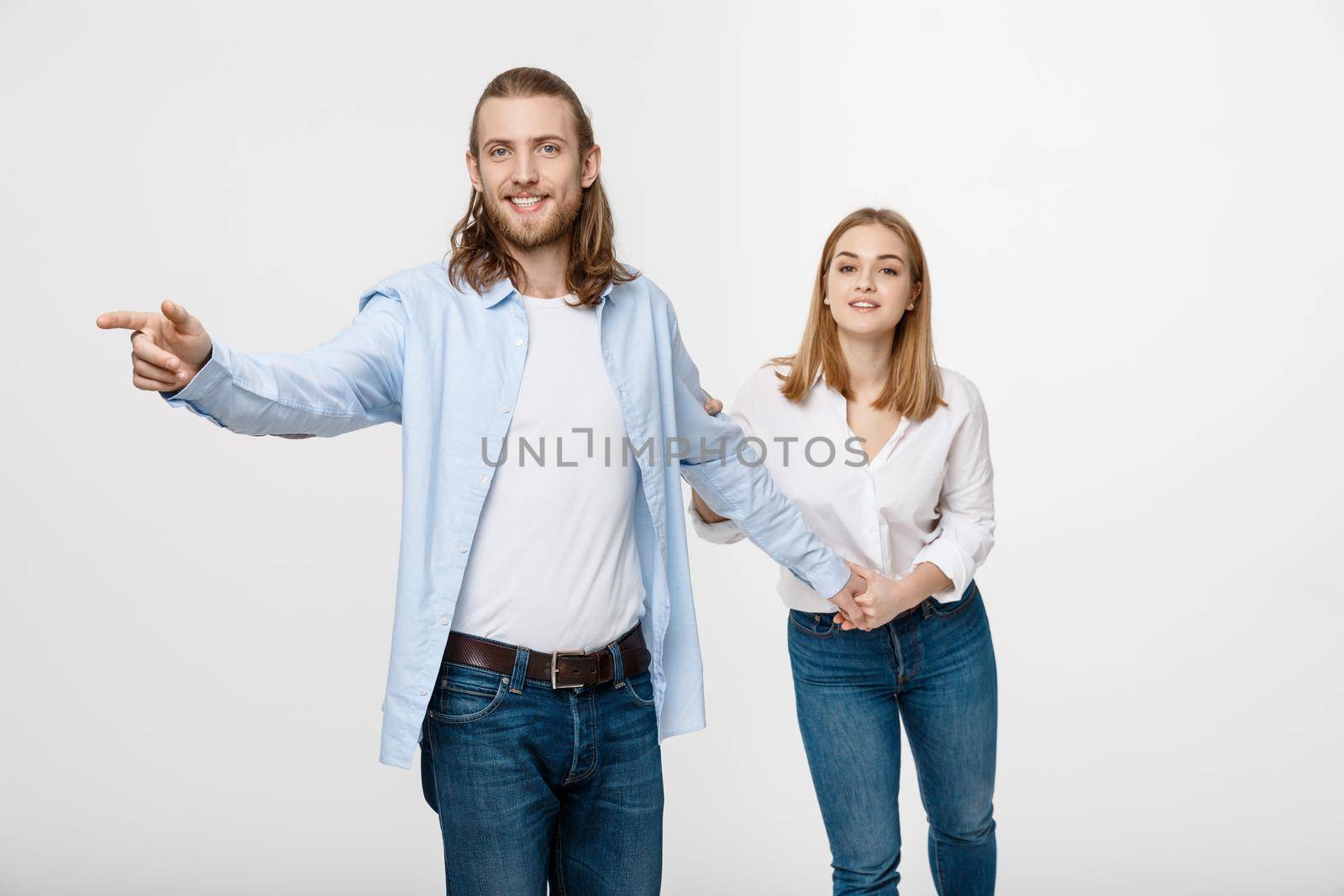 Portrait young happy couple love smiling embracing point finger to empty copy space, man and woman smile looking up, isolated over white background.