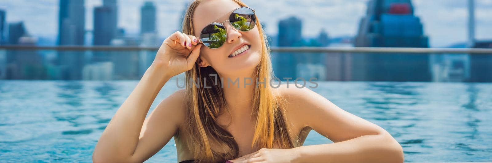 Young woman in outdoor swimming pool with city view in blue sky. BANNER, LONG FORMAT