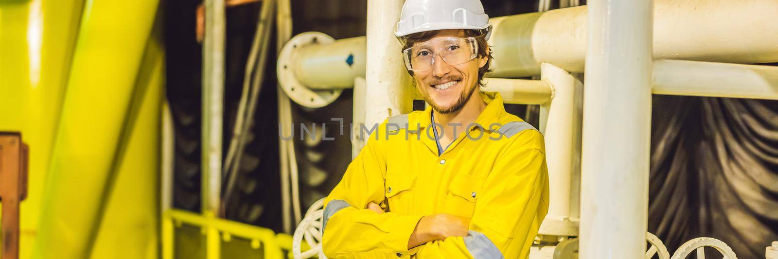 Young man in a yellow work uniform, glasses and helmet in industrial environment,oil Platform or liquefied gas plant. BANNER, LONG FORMAT