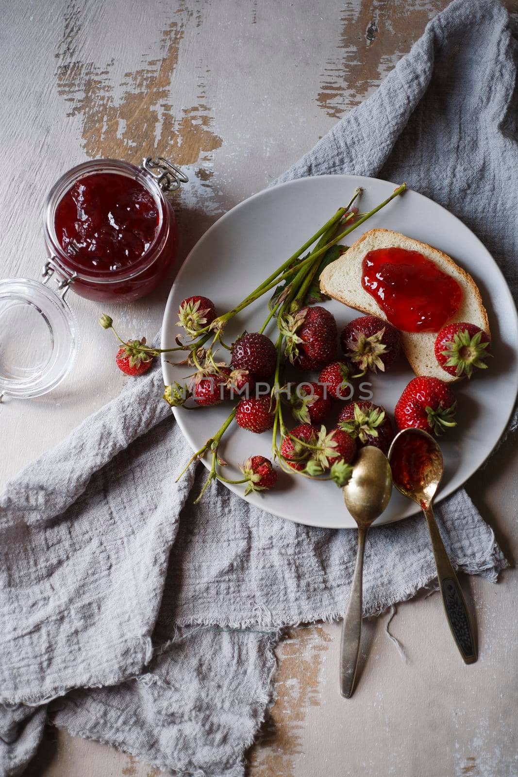 Summer breakfast concept with srawberry jam with bread and fresh harvested berries on gray plate, flat lay, selective focus.