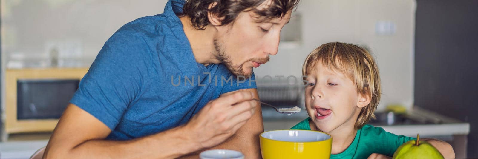 Father and son are talking and smiling while having a breakfast in kitchen. BANNER, LONG FORMAT