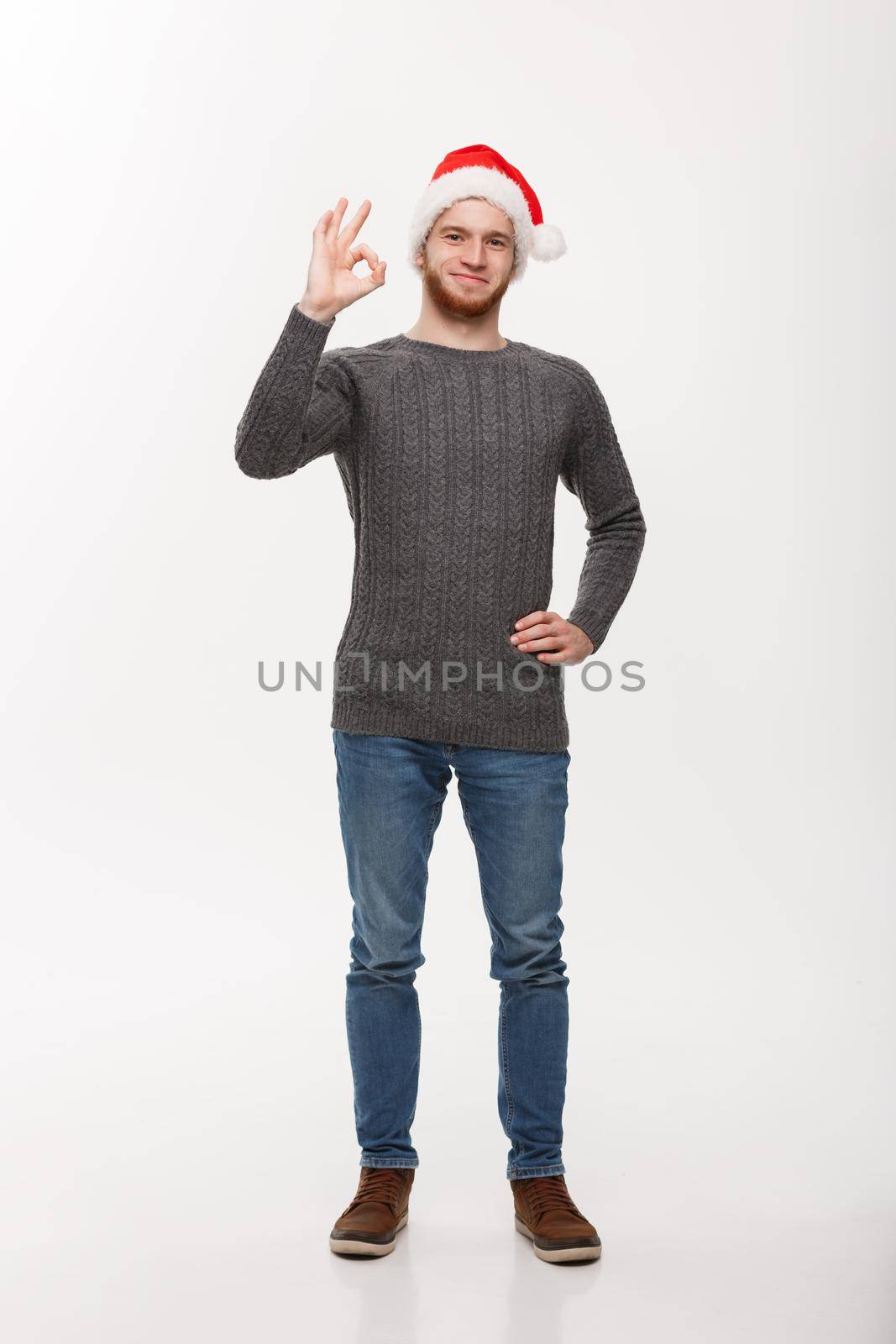 Holiday Concept - Young beard man in sweater giving ok sign to camera.