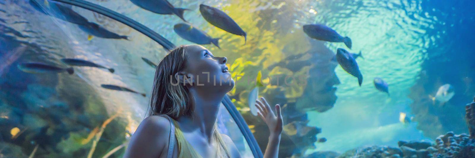 Young woman touches a stingray fish in an oceanarium tunnel. BANNER, LONG FORMAT