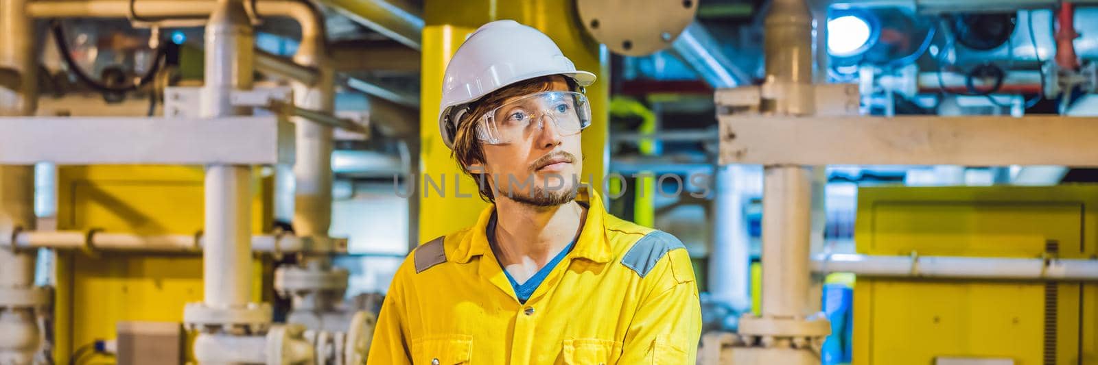 Young man in a yellow work uniform, glasses and helmet in industrial environment,oil Platform or liquefied gas plant. BANNER, LONG FORMAT