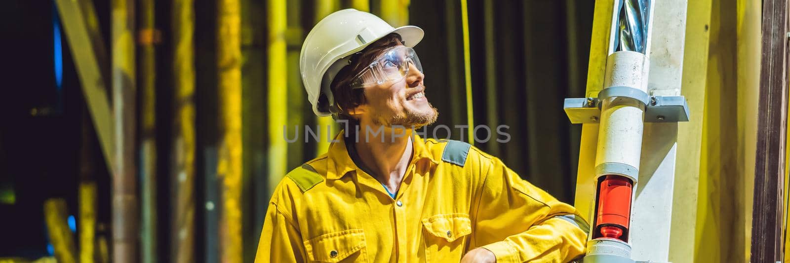 Young man in a yellow work uniform, glasses and helmet in industrial environment,oil Platform or liquefied gas plant. BANNER, LONG FORMAT