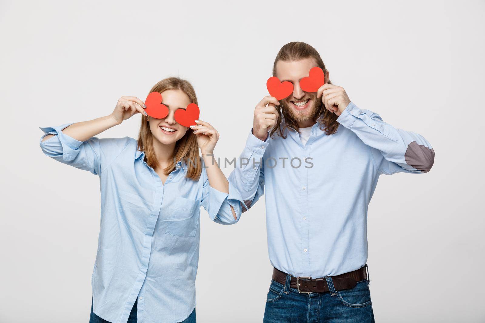 Attractive young in love couple holding red hearts over eyes on white background.
