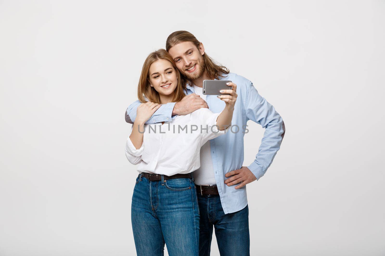 Portrait of a happy couple making selfie photo with smartphone over isolated white studio background